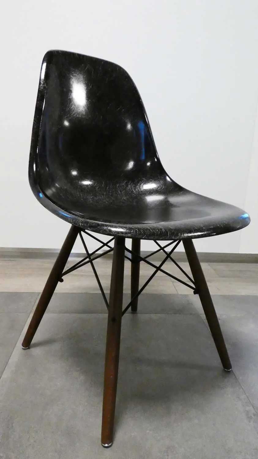 Glanzende zwarte schaalstoel met donkere houten poten en metalen verstevigingsdraden op een grijze tegelvloer.