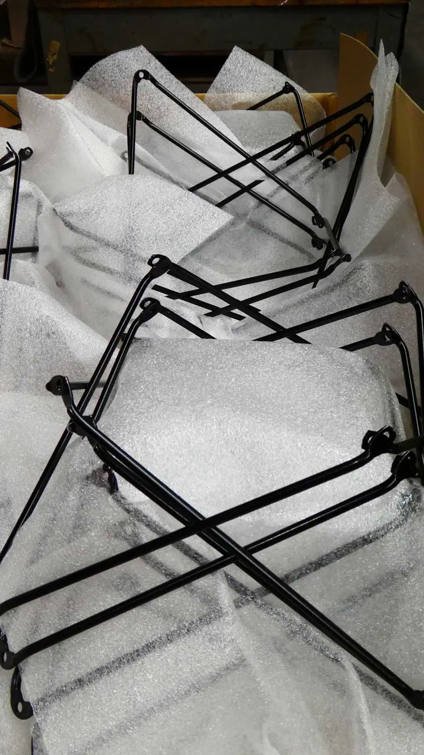 Zwarte gelakte metalen stangenframes liggen verpakt in wit schuimfolie in een houten krat.