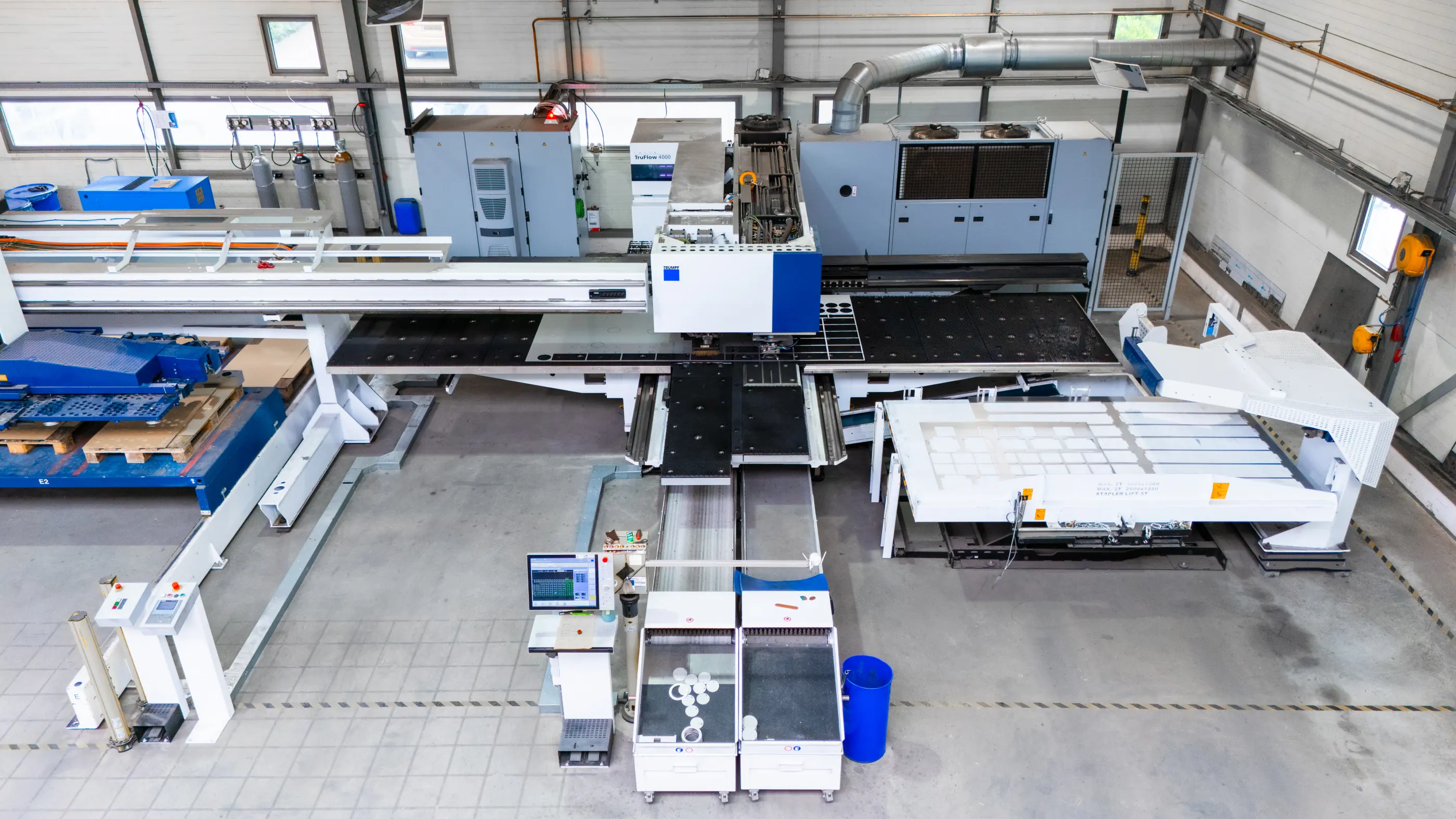 Bovenaanzicht van een grote CNC-ponsmachine met bedieningsscherm en sorteerbakken in een lichte industriële productiehal.